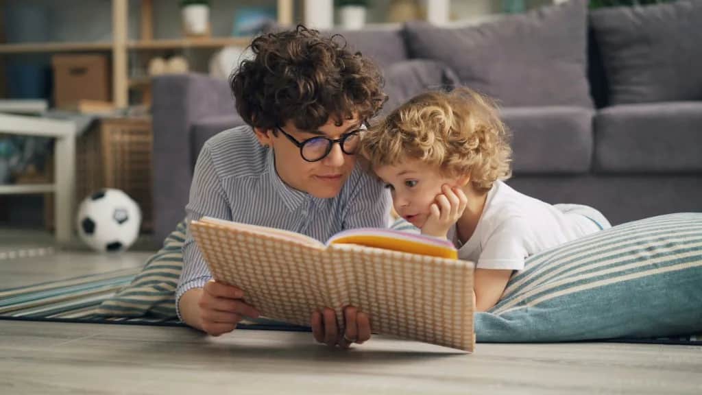 Una adulta y un niño leen juntos tumbados en el suelo, concentrados en el libro.