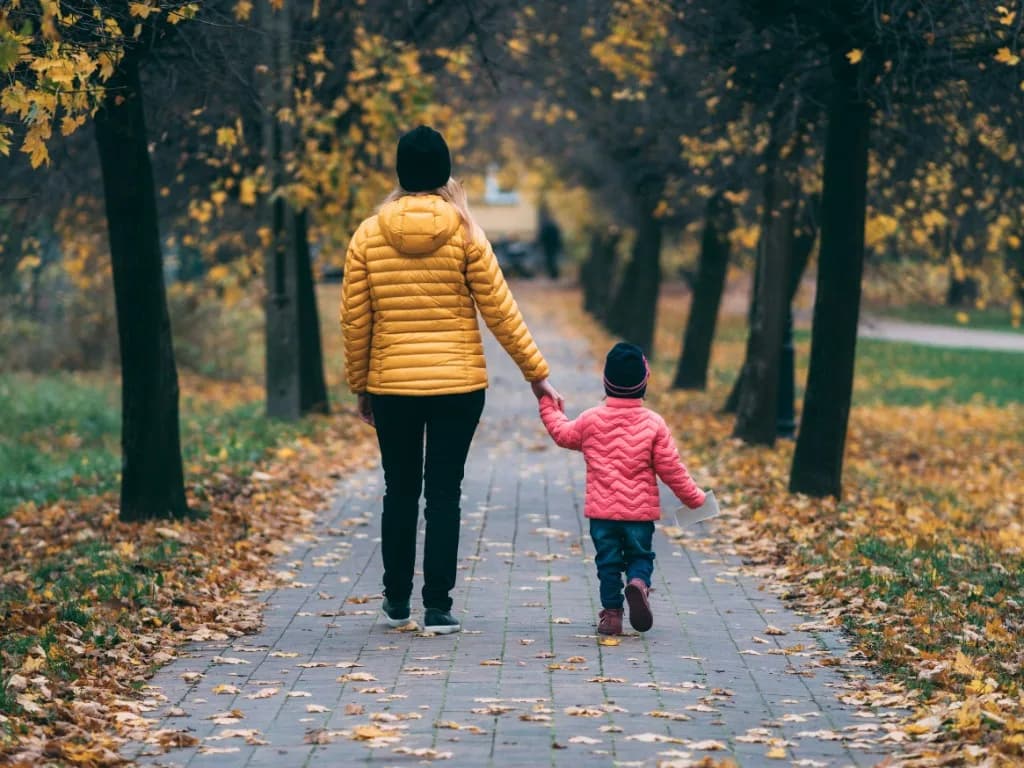 Un adulto y un niño caminan de la mano por un parque en otoño.