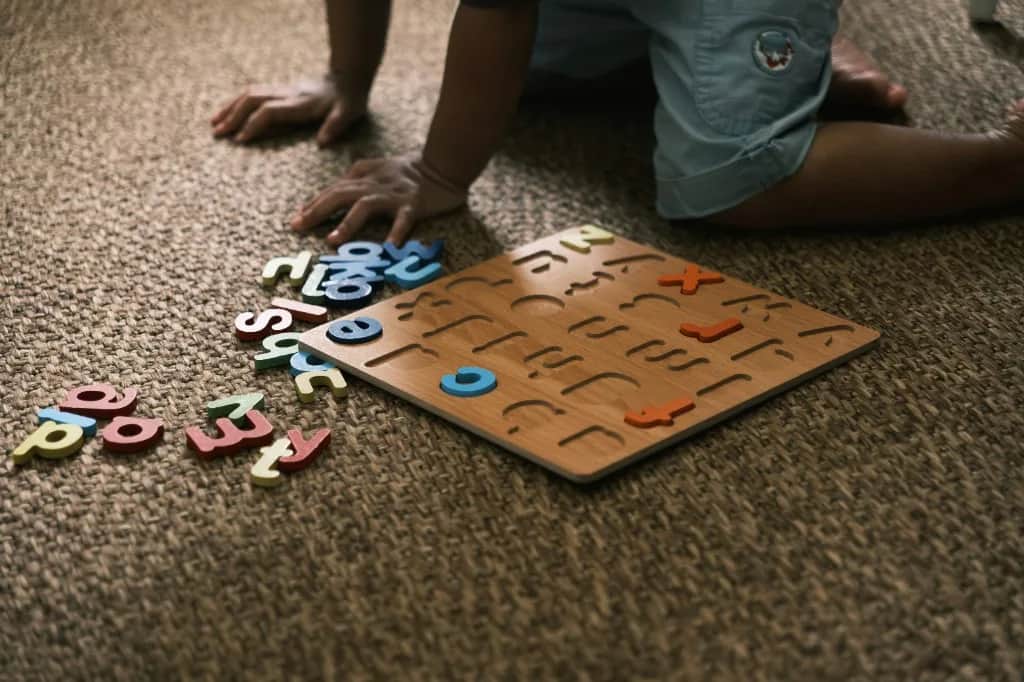 Puzzle de letras de madera sobre la alfombra, con las manos de un niño al fondo.