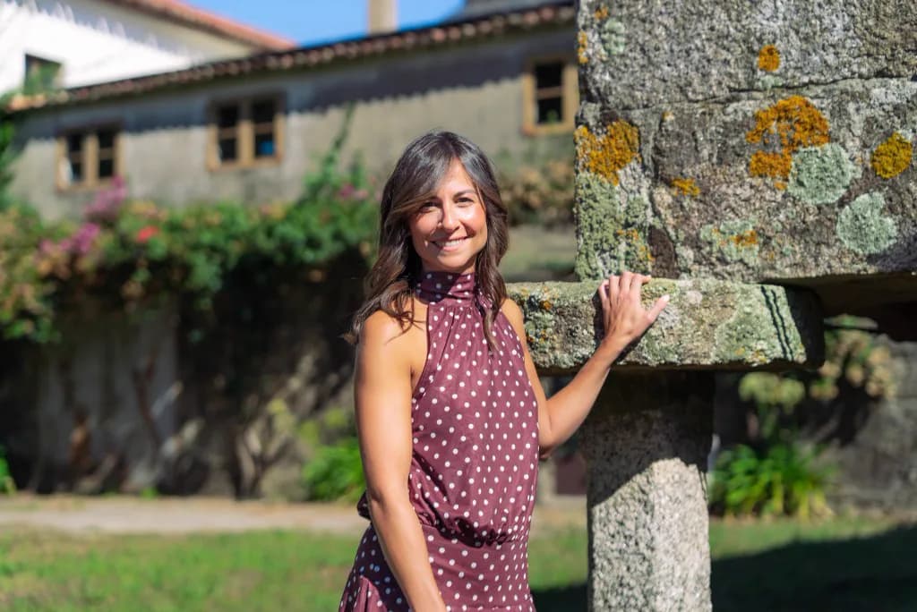 Paula Cid sonríe apoyada en un hórreo gallego, con un vestido de lunares.