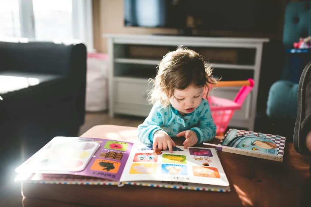Una niña pequeña señala dibujos en un libro ilustrado abierto.